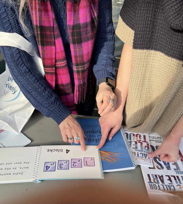 Two visitors examine a book in both print and Braille