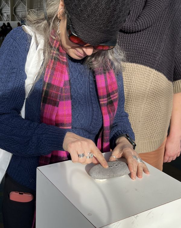 A visitor reads Braille dots on a stone