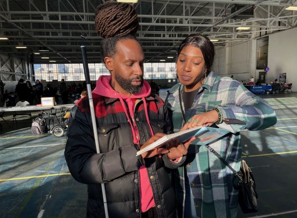 Two visitors, one blind and one sighted, examine a children's book in both print and Braille