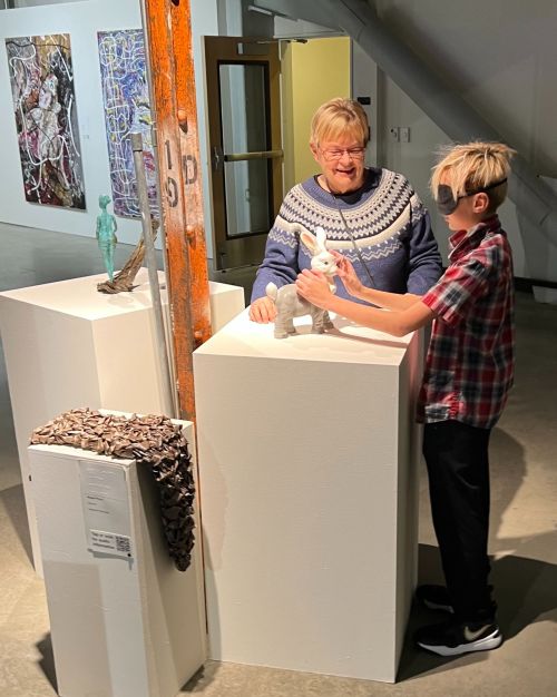 A blindfolded youth feels a sculpture at Please Touch 2024