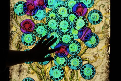 Hand touching a glass work depicting flowers